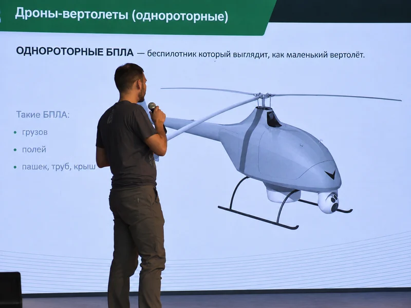 Преподаватель у экрана с учебной презентацией о беспилотниках.